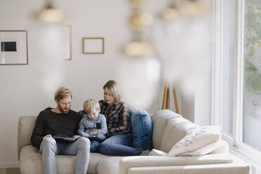 Familie schaut sich auf der Couch zu Hause ein Buch an - KNSF07142