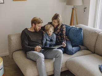 Familie schaut sich auf der Couch zu Hause ein Buch an - KNSF07143