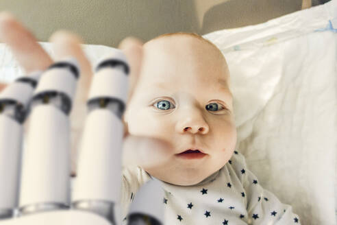 Portrait of baby boy reaching for robot hand - KSHSF00019