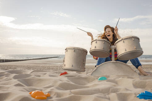 Porträt einer lachenden Frau, die am Strand Schlagzeug spielt - KSHSF00021