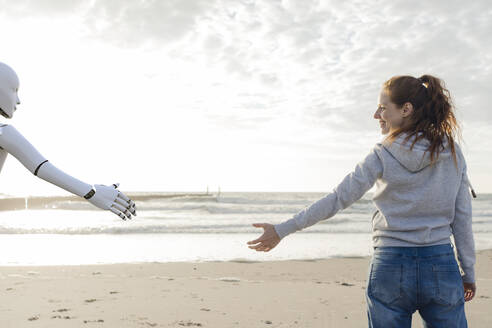 Lächelnde Frau am Strand, die nach der Hand eines Roboters greift - KSHSF00027