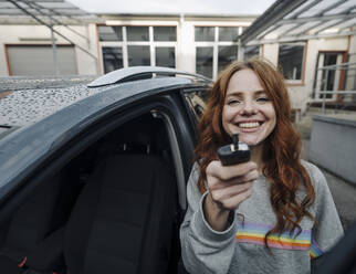 Portrait of happy redheaded woman beside car holding key - KNSF07145