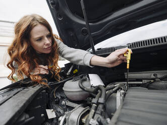 Rothaarige Frau prüft das Motoröl ihres Autos - KNSF07150