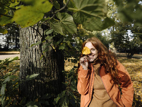 Portrait of happy redheaded woman holding autumn leaf stock photo