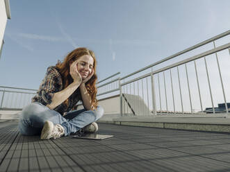 Rothaarige Frau mit Tablet entspannt sich auf einer Dachterrasse - KNSF07160