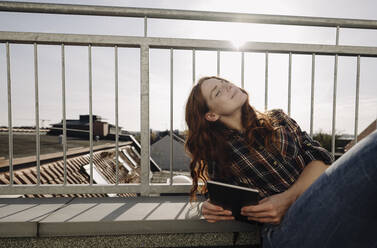 Redheaded woman with tablet relaxing on rooftop terrace - KNSF07161