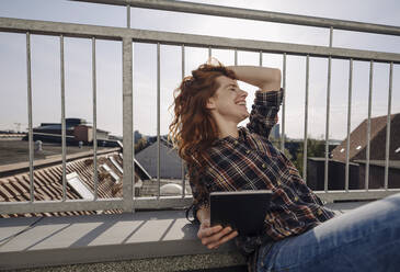 Glückliche rothaarige Frau mit Tablet entspannt auf Dachterrasse - KNSF07162