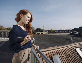 Lächelnde rothaarige Frau mit Tablet auf einer Dachterrasse - KNSF07168