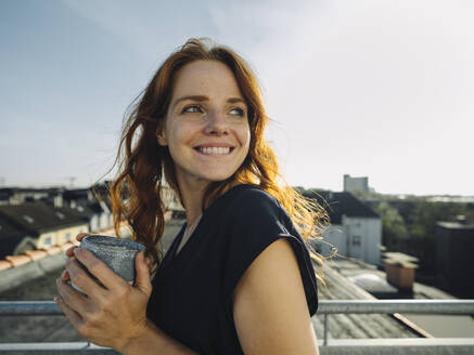 Lächelnde rothaarige Frau bei einer Kaffeepause auf der Dachterrasse - KNSF07172