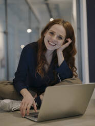 Portrait of smiling redheaded woman using laptop on the floor - KNSF07177