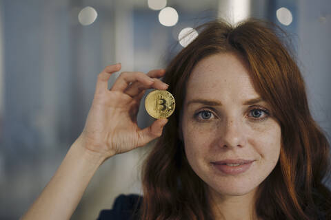 Porträt einer rothaarigen Frau mit Bitcoin in der Hand, lizenzfreies Stockfoto