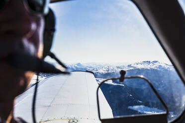 Österreich, Tirol, Steinberg am Rofan, Pilot schaut durch das Fenster während des Fluges über das Gebirge - DHEF00065