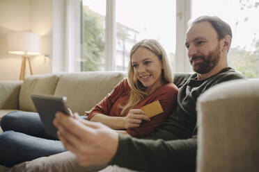 Couple sitting at home on couch, using digital tablet - KNSF07186