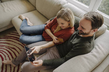 Ehepaar sitzt zu Hause auf der Couch und benutzt ein digitales Tablet - KNSF07187