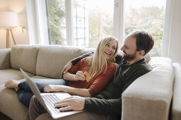 Couple sitting at home on couch, using laptop - KNSF07188
