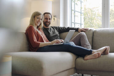 Couple sitting at home on couch, using laptop - KNSF07191