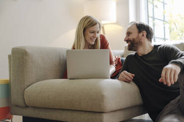Ehepaar sitzt zu Hause auf der Couch und benutzt einen Laptop - KNSF07192