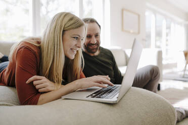 Ehepaar sitzt zu Hause auf der Couch und benutzt einen Laptop - KNSF07193