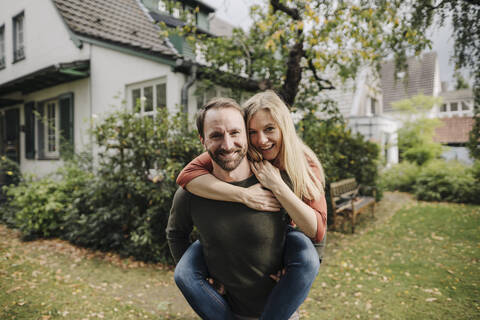 Mann trägt glückliche Frau huckepack im Garten, lizenzfreies Stockfoto