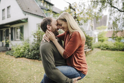 Happy couple kissing in garden, in front of their dream house - KNSF07222