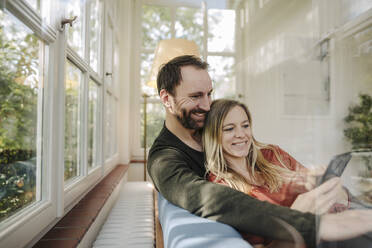 Happy couple relaxing on couch, using smartphone - KNSF07234