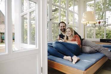 Happy couple relaxing on couch, using smartphone - KNSF07235