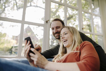 Laughing couple using smartphone at home - KNSF07236