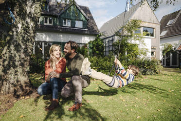 Son swinging in garden with parents next to him - KNSF07243