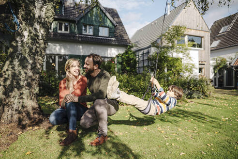 Sohn schaukelt im Garten mit Eltern neben ihm - KNSF07243