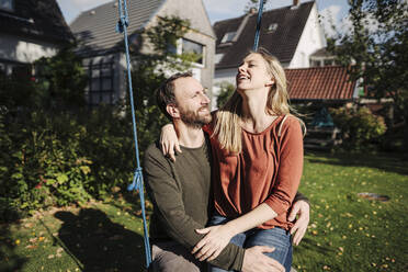 Affectionate couple sitting on swing in in their garden - KNSF07244