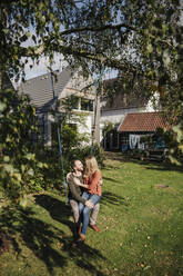 Affectionate couple sitting on swing in in their garden - KNSF07246