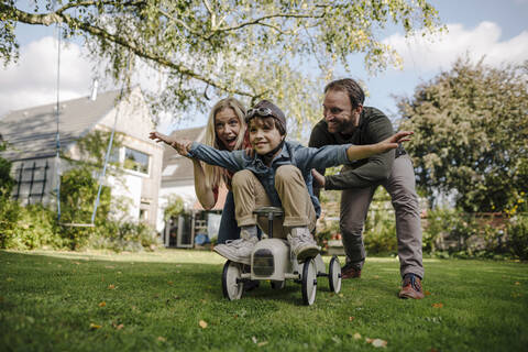 Boy sitting on toy car, pretending to fly, parents encourageing him stock photo