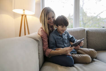 Mutter und Sohn sitzen auf der Couch und benutzen ein digitales Tablet - KNSF07260