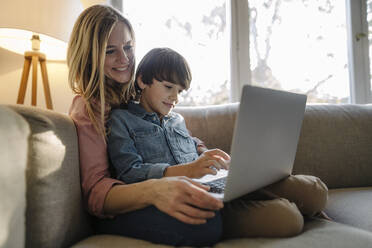 Mother and son sitting on couch, using laptop - KNSF07261