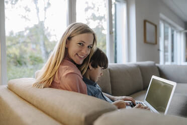 Mutter und Sohn sitzen auf der Couch und benutzen einen Laptop - KNSF07262