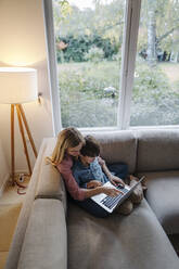 Mother and son sitting on couch, using laptop - KNSF07263