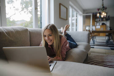 Frau auf Couch liegend, mit Laptop - KNSF07264