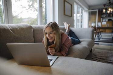 Frau auf Couch liegend, mit Laptop - KNSF07265