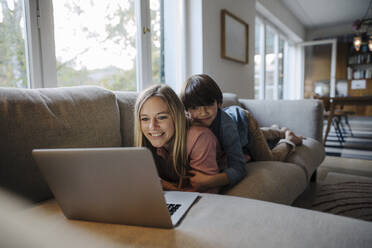 Mother and son lying on couch, using laptop - KNSF07266