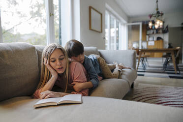 Mother and son lying on couch, using reading book - KNSF07267