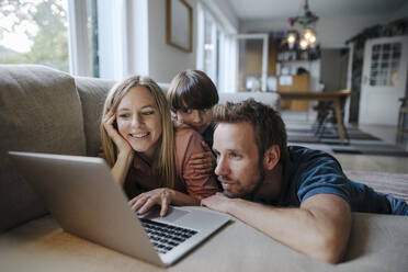 Glückliche Familie auf der Couch liegend, mit Laptop - KNSF07268