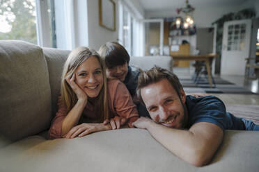 Happy family lying on couch, smiling at camera - KNSF07269