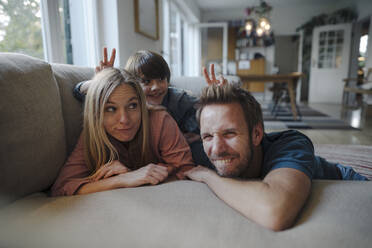 Happy family lying on couch, son making fun of his parents - KNSF07270