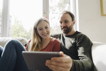 Ehepaar sitzt zu Hause auf der Couch und benutzt ein digitales Tablet - KNSF07282