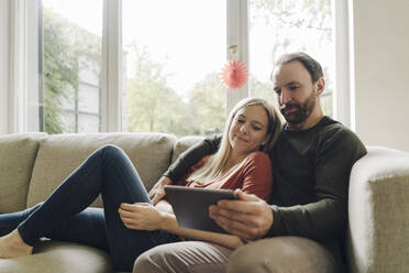 Couple sitting at home on couch, using digital tablet - KNSF07283