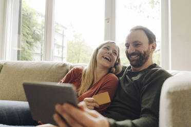 Ehepaar sitzt zu Hause auf der Couch und benutzt ein digitales Tablet - KNSF07284