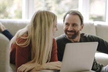 Couple sitting at home on couch, using laptop - KNSF07287