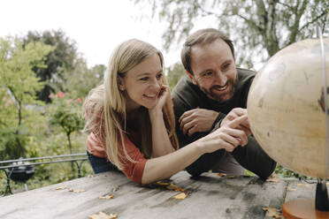 Happy couple planning to travel, looking at globe outdoors - KNSF07302