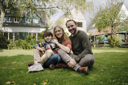 Happy family sitting on grass in their garden - KNSF07317