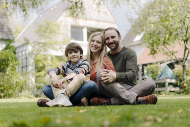 Happy family sitting on grass in their garden - KNSF07318